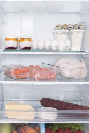 in the open refrigerator, on glass shelves, there are products, whole chicken, meat, eggs, cheese, sausage, cottage cheese, yogurt and vegetablesの写真素材