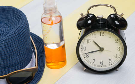 on a gray-yellow surface, a sun protection kit, a hat, glasses and an alarm clock, close-upの写真素材