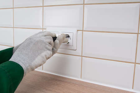 the electrician mounts the socket in the wall, twists it with a screwdriverの写真素材