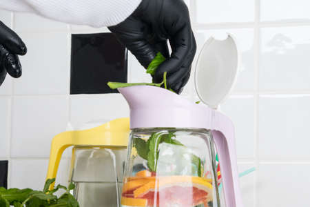 the process of adding mint to a glass jug with a refreshing drink, by the hands of a chef, against the background of a black and white kitchenの写真素材