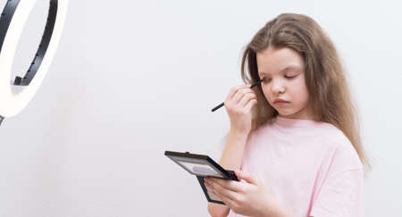 girl blogger, in front of a circular light, makes a make-up, applies shadows on the eyelidsの写真素材