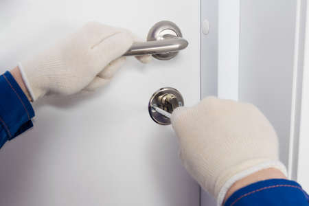 the hands of the foreman mending the lock of the white front door, close-upの写真素材