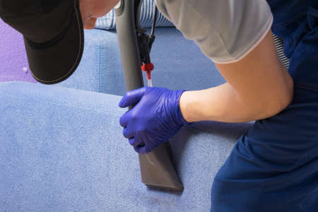 vacuum cleaner brush picks up foam from blue sofa, cleaning company employee, top viewの写真素材