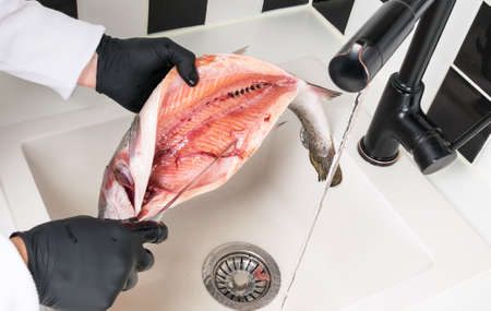 the hands of the chef wash the red fish under running waterの写真素材