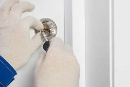 the hands of the master install the lock on the white front door, close-upの写真素材