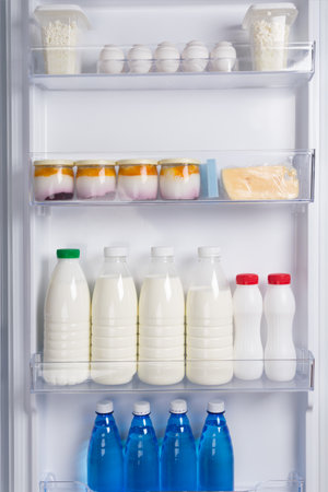 in the door of the white refrigerator, on the shelf are eggs, cheese, yogurt, cottage cheese, milk and bottled waterの写真素材