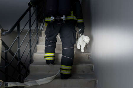 a firefighter climbs the stairs in incomplete darkness, holding a child's toy in his handの写真素材