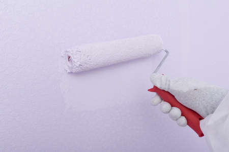 a painter's hand in protective gloves, with a large roller, painting a white wall in a light purple colorの写真素材