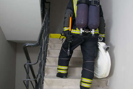 rear view of a firefighter who climbs with equipment sleeves and an ax, wearing a breathing apparatus along an internal evacuation ladderの写真素材