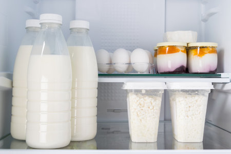 against the background of a white refrigerator, on glass shelves are products, milk, eggs, cottage cheese and yogurt, close-upの写真素材
