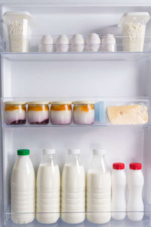 in the door of the white refrigerator, on the shelf are eggs, cheese, yogurt, cottage cheese and milk in bottlesの写真素材