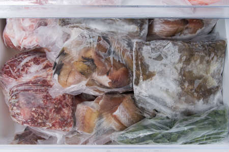 a close-up of a refrigerator drawer containing frozen meat and fish in packing bagsの写真素材