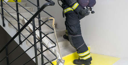 the firefighter unscrews the valve of the air apparatus of one of the cylinders, going up the stairsの写真素材