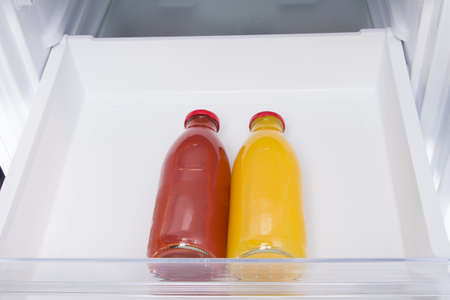 against the background of a white refrigerator drawer, two glass bottles with juice, close-upの写真素材