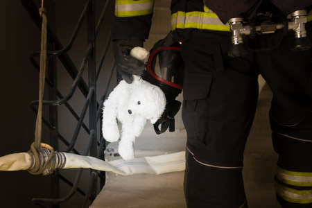 a firefighter climbs the stairs in incomplete darkness, holding a child's toy in his hand, close-upの写真素材