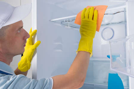 a man from the cleaning service in protective gloves, wiping the refrigerator with a rag, close-upの写真素材
