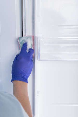 the hand of a cleaning service worker in a protective glove wipes the refrigerator with a sponge with cleaning foamの写真素材