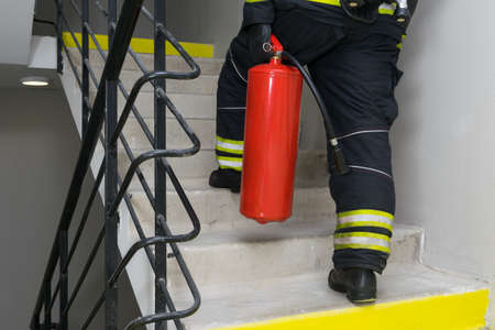 rear view of a firefighter who climbs with a fire extinguisher along the internal escape stairsの写真素材