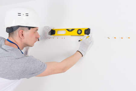 a builder in a protective helmet, marks out with the help of a level, a place under the holeの写真素材