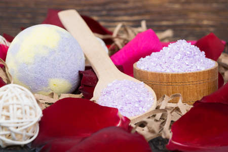 on a dark wooden background, surrounded by rose petals, in a container and on a spoon, fragrant bath salt and a relaxation bombの写真素材