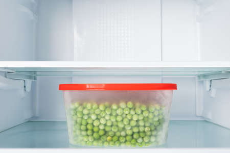 a container of fresh peas on a shelf in an empty refrigeratorの写真素材