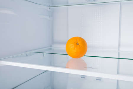 an orange on a shelf in an empty fridgeの写真素材