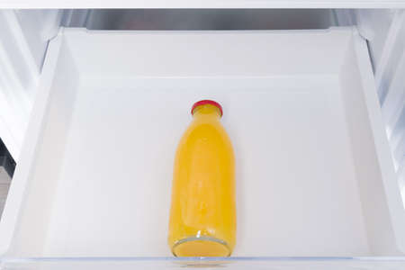 against the background of a white refrigerator drawer, one glass bottle with orange juice, close-upの写真素材