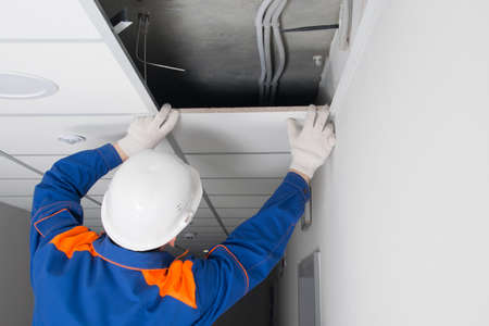 the master of installation of suspended ceilings, completes the assembly of plates on a metal frame, rear viewの写真素材