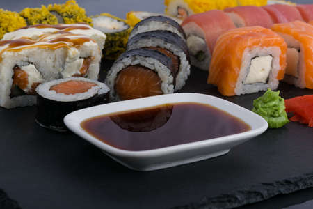 on a black table, assorted Japanese salmon and tuna rolls, next to seasonings soy sauce, wasabi and pickled gingerの写真素材