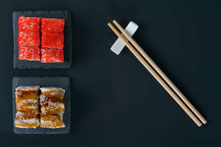 on a black table, top view, rolls with eel, teriyaki sauce, sesame seeds, flying fish caviar and...