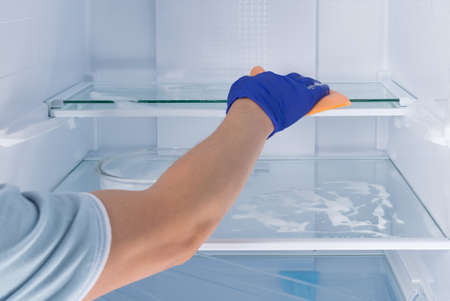 the hand of a cleaning service worker in a protective glove, wipes the glass shelves of the refrigerator with a sponge with cleaning foamの写真素材
