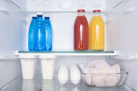 against the background of a white refrigerator, on the shelves, there are products, whole chicken, eggs, cottage cheese, bottled water and juicesの写真素材
