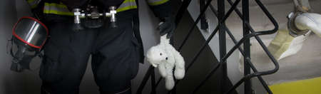 a firefighter walks down the stairs holding a teddy bear toy in his handの写真素材