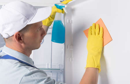 the cleaner wipes the white refrigerator with a yellow clothの写真素材
