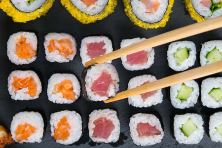 on a black table, assorted rolls, with salmon, tuna and cucumber, laid out in a row, wooden sticks take oneの写真素材