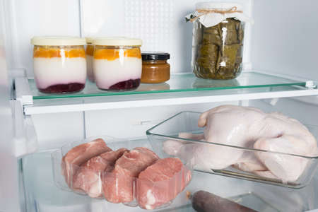 meat and dairy products are on a shelf in an open refrigeratorの写真素材