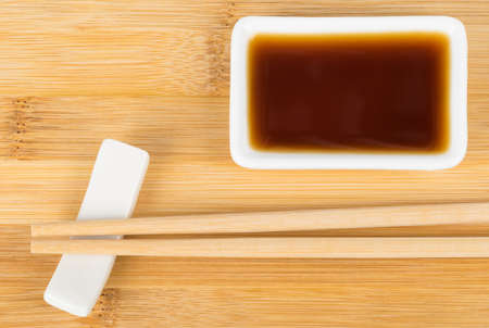 sushi sticks and soy sauce in a white bowl on a wooden boardの写真素材