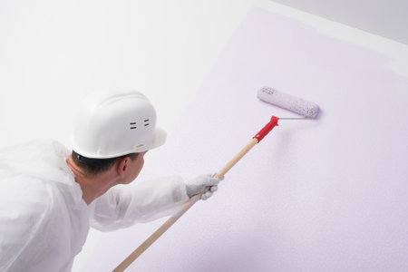 a worker in a hard hat paints a white wall with a roller in lilac color, rear viewの写真素材