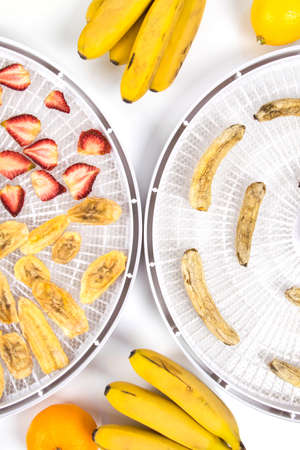 chopped pieces of bananas and strawberries, on round grates after drying, in special equipment, on a white table, surrounded by fresh whole fruitsの写真素材
