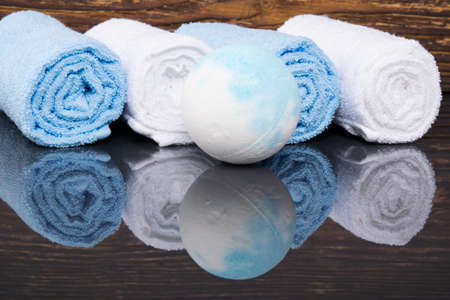 on a dark wooden background with reflection, spa towels wrapped in a roll and a ball of saltの写真素材