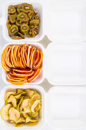 in plastic white containers there are dried fruits, apple, kiwi and grapefruit, close-up, with places for the inscriptionの写真素材