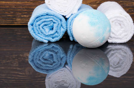 on a dark wooden background with reflection, blue bath salt in the form of a relaxation bomb and towels wrapped in a rollの写真素材