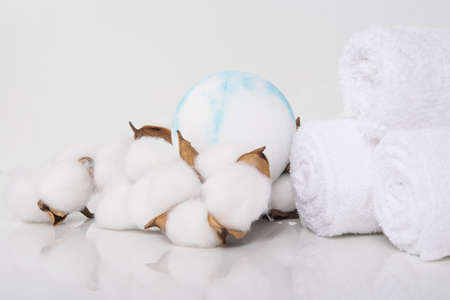 on a white table with a reflection, towels rolled up for spa treatments and bath salts in the form of a ball, close-upの写真素材