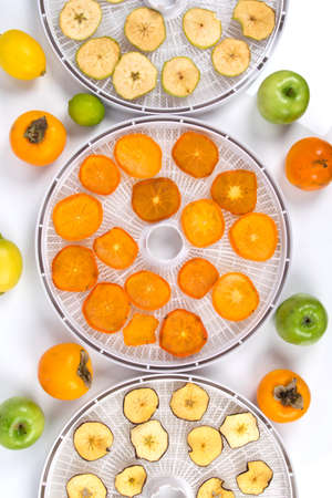 sliced pieces of apples and persimmons, on grates after drying, in special equipment, surrounded by fresh fruits, top viewの写真素材