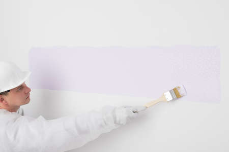 a man with a roller starts painting a white wall in a different colorの写真素材