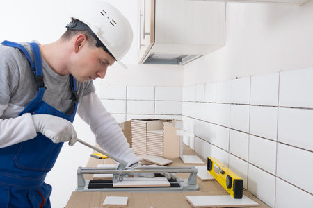 a man in a helmet and gloves, engaged in cutting tiles, for laying on the wallの写真素材