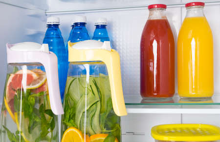 against the background of a white refrigerator, on the shelves are soft drinks, citrus lemonade in a jug, bottled water and juicesの写真素材