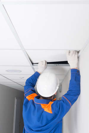 a master in a protective helmet, for the installation of suspended ceilings, completes the assembly of plates, rear viewの写真素材