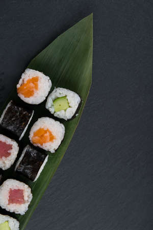 on a dark table, on a bamboo leaf, assorted Japanese delicacies, cucumber and fish rolls, there is a place for the inscriptionの写真素材