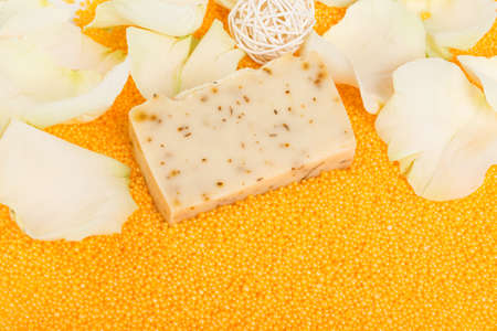 close-up, a piece of handmade soap on scattered orange bath salts in the form of small balls, surrounded by white rose petalsの写真素材